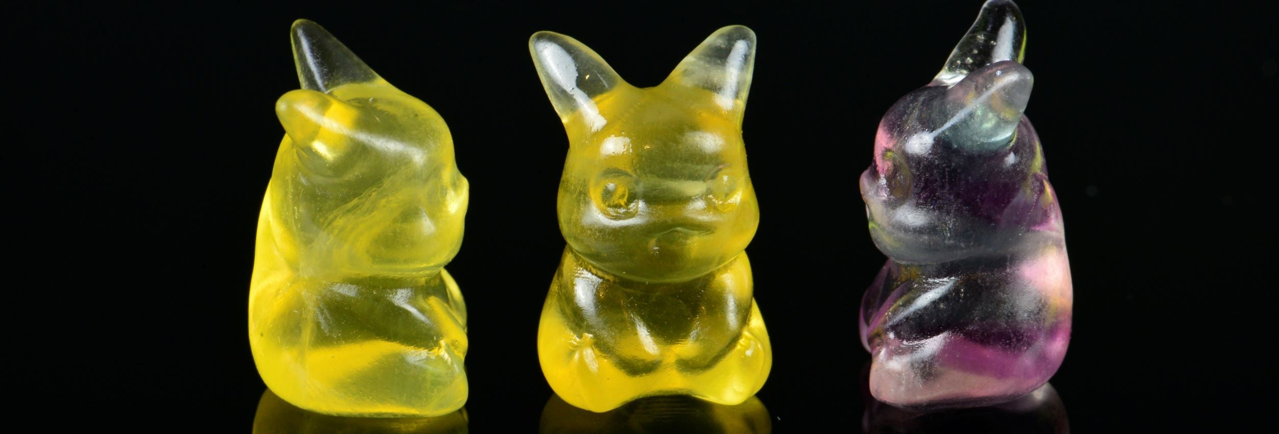 3 colourful fluorite pikachu pokemon carvings on a black background